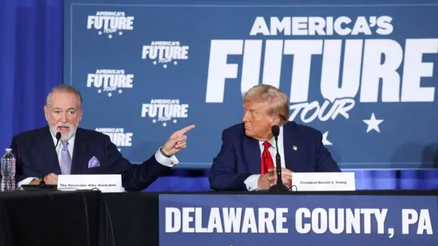 Mike Huckabee speaks as Donald Trump looks at him during a campaign event at the Drexelbrook Catering and Event Center, in Drexel Hill, Pennsylvania