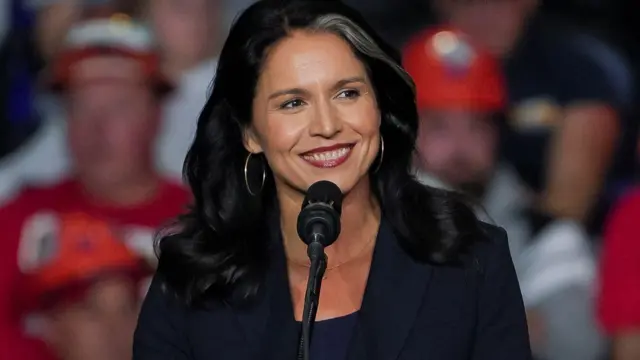 Tulsi Gabbard smiling in front of a podium at a Donald Trump rally