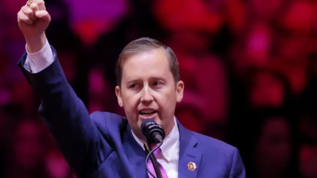 Gor raises his hand in a fist as he speaks at a lectern