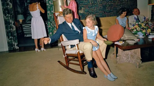 Then US President John F Kennedy sitting in a rocking chair with his daughter, Caroline Kennedy