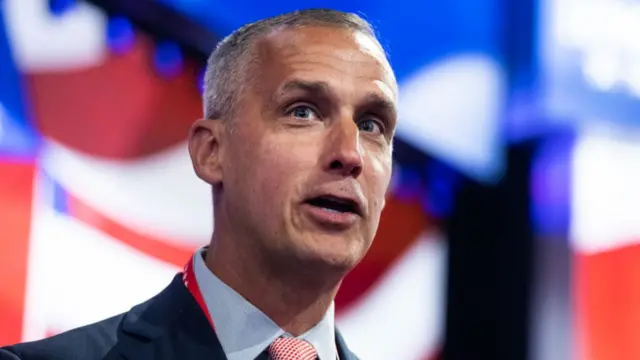 Former Trump aide Corey Lewandowski is seen in close up. He has grey hair and is seen against a blue and red backdrop