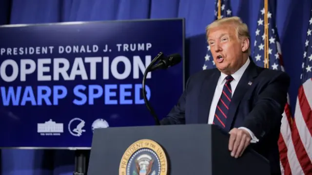 Donald Trump stood in front of a lectern, with a screen behind him which says: "OPERATION WARP SPEED".