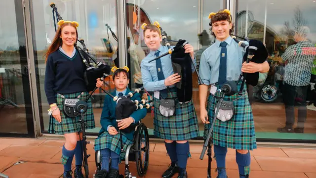 Four young musicians in Scottish clothing pose with their bagpipes