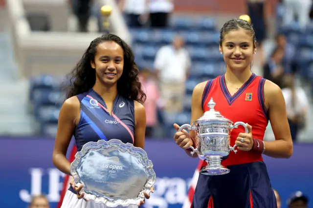 Leylah Fernandez of Canada holds the runner-up trophy as Emma Raducanu of Great Britain celebrates