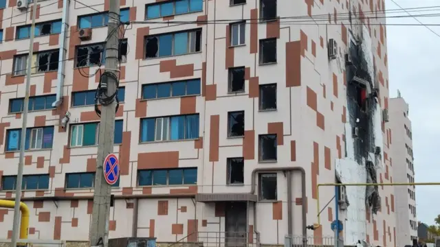 A multi-storey building with a blackened hole on one side and windows smashed