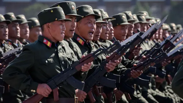 Soldiers holding guns and dressed in dark green military uniform march in a parade