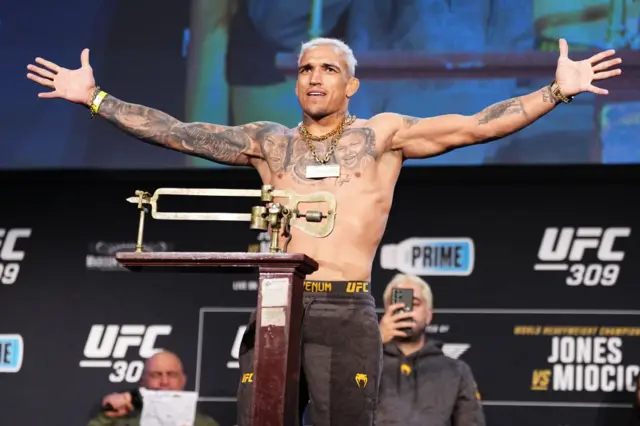 Charles Oliveira holds out his arms and stands on the scales