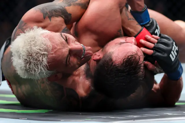 Charles Oliveira sticks his tongue out as he grapples with Michael Chandler