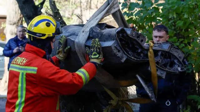 Worker standing next to a piece of a Russian missile which is being lifted in a harness in Kyiv