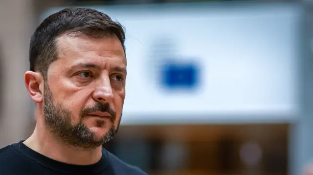 A file photo of Volodymyr Zelensky. He's on the left of the frame looking to his left, shot cuts below the neck. He's in a black shirt