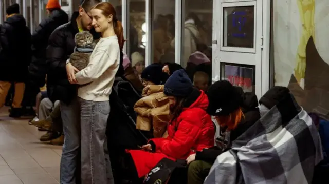 People seek shelter in a Kyiv metro station, some wrapped in blankets, one woman carrying a cat