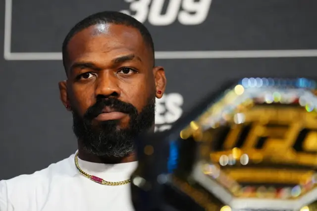 Jon Jones sits next to the UFC heavyweiht title