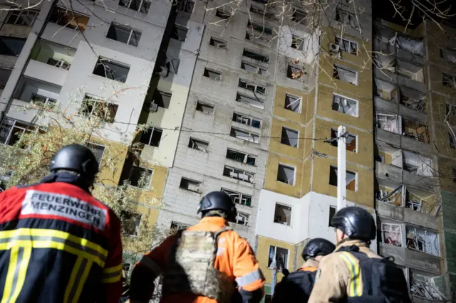 Firefighters stand at the bottom of a residential building in Sumy, that was hit by Russian strikes