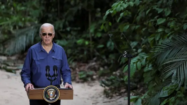 Joe Biden stands at a podium against a backdrop of the rainforest