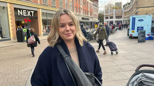 Emma Taylor standing in the street in Cambridge, near the market square, with shops and shoppers in the background