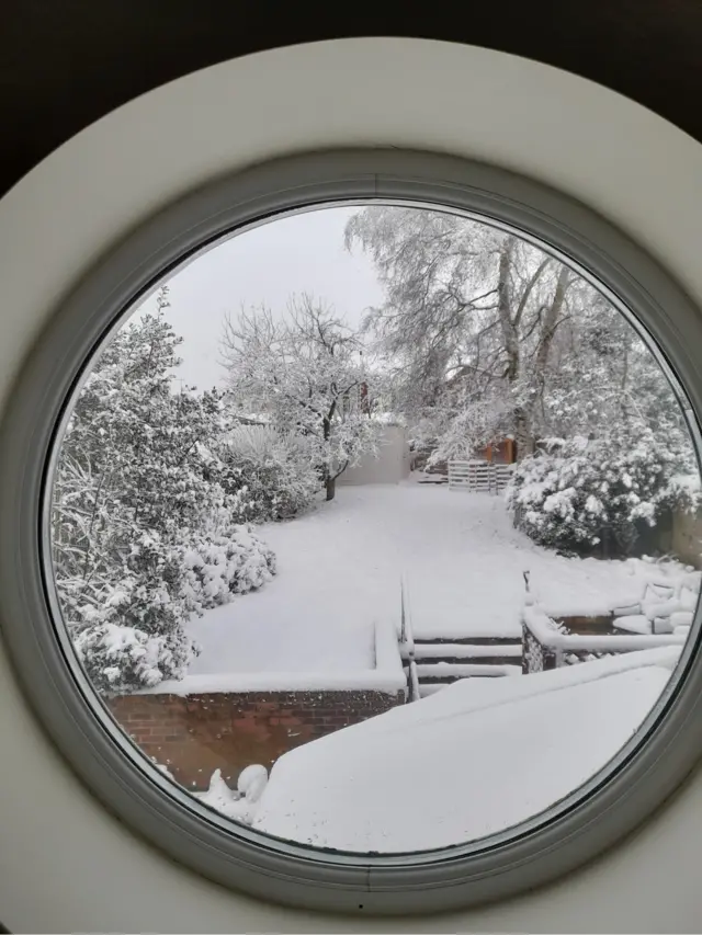 A snow covered garden through a round window