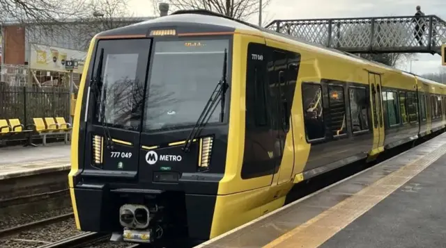 Train on a Merseyrail railway station with a person walking on a bridge in the background