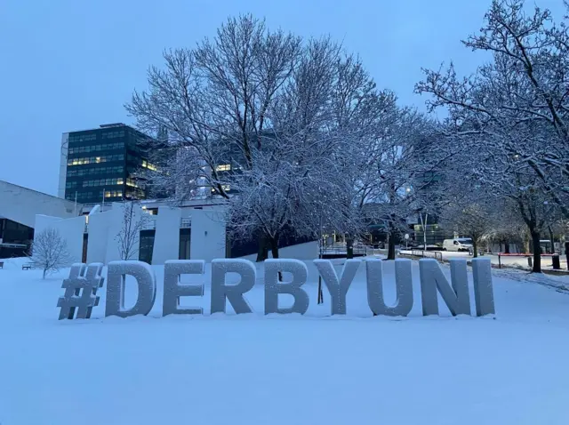 A sign saying "#DerbyUni" in the snow