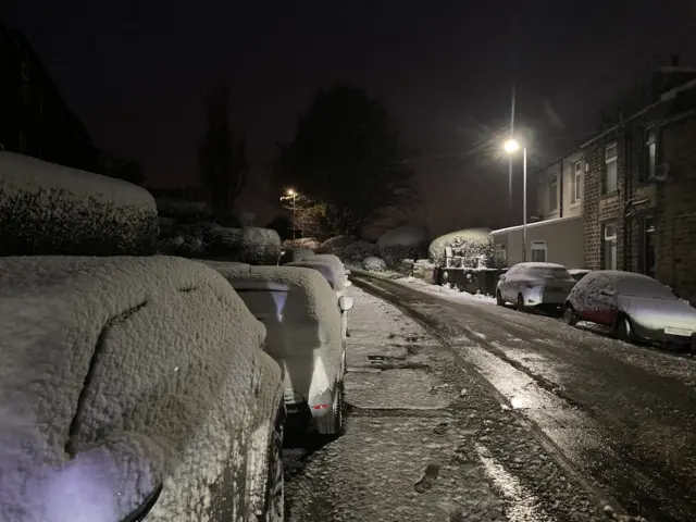 Snow-covered cars down a dimly-lit street