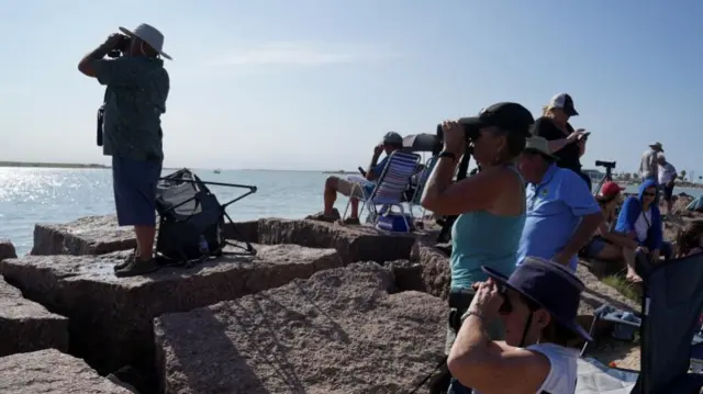 People staring across water with binoculars raised