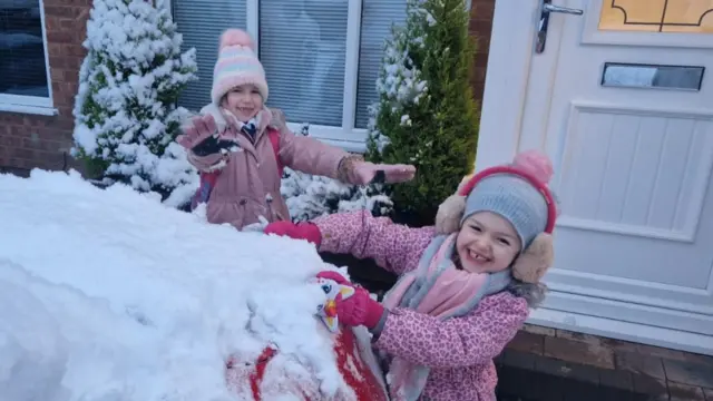 Two girls playing with snow on car