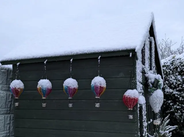 A snow-covered shed with balloon decorations covered in snow hanging from it