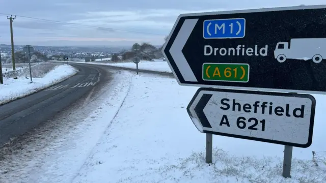 Road signs poiting to Dronfield and Sheffield at the junction of a snowy road