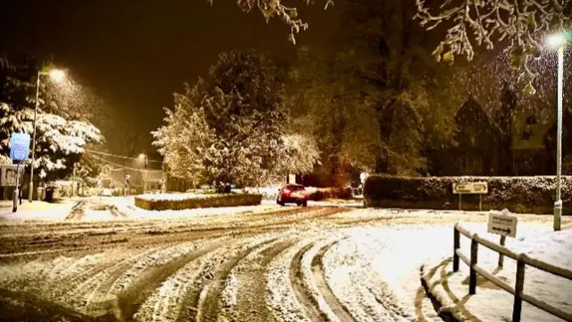 A snowy road in the dark with some car tracks in the snow