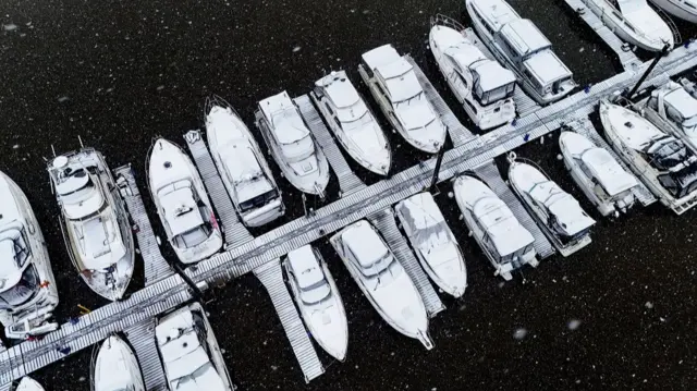 Snow-covered boats seen from above on the water in Upton.  A snow-covered jetty can be seen running between the boats.