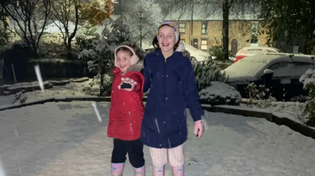 Two children standing in a snowy garden and smiling in their coats