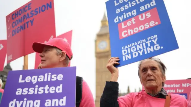 Two people holding up signs that support the assisted dying bill