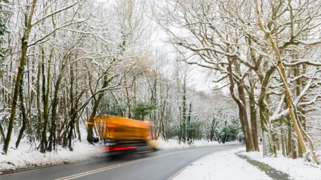 Country road covered in snow with gritter vehicle travelling on the road laying salt down