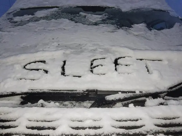 A snow-covered car with the word 'sleet' written in the snow on the bonnet