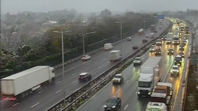 Traffic on a motorway in both directions with slush on either side of the motorway. Lorries and cars can be seen queuing on one side