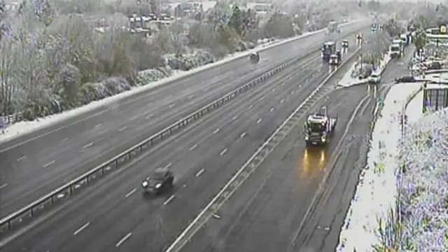 Some cars on a motorway with snow on either side of the carriageways