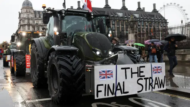 Protesters drive tractors through Westminster. It is adorned with a sign that reads 'The Final Straw'