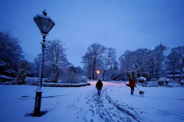 A woman walks a dog through the overnight snow in a park in Buxton, Derbyshire