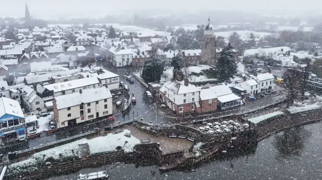 Snow falling in Upton-upon-Severn in Worcestershire. The river can be seen in the foreground with snow-covered buildings stretching away to the eye