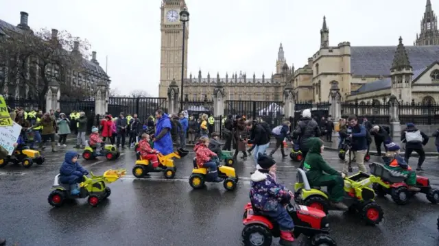 Dozens of children on mini tractors drive past Parliament Square in front of Big Ben