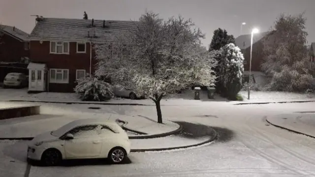 A snowy sttreet in Tipton with a light covering of snow over cars and houses