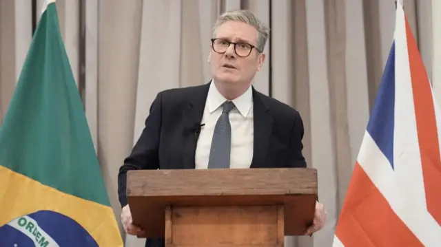 Keir Starmer speaking at a podium. There is a Brazil flag and a British flag on either side of him