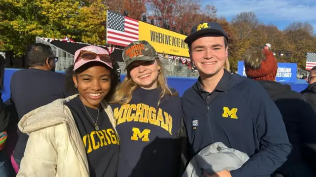 Hannah Brocks, Alannah Hjelm and Luke Meijer at a Kamala Harris rally in Michigan. All three wear sweaters featuring the University of Michigan's logo.