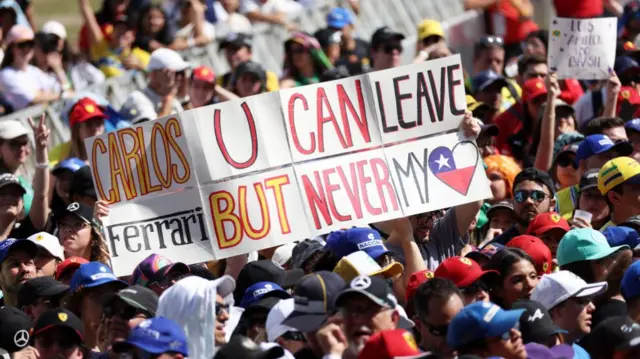 fan holds up a sign reading Carlos you can leave ferrari but never my heart