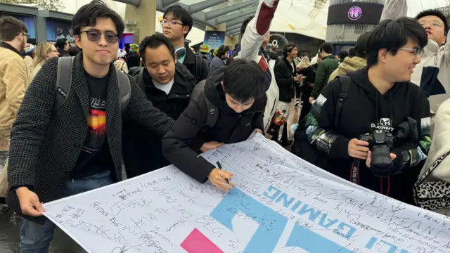 Four men gather around a flag bearing the letters BLG, with one of them signing it