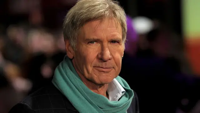 Harrison Ford, pictured at a movie premier in London wearing a black coat with a teal green scarf, in 2011.