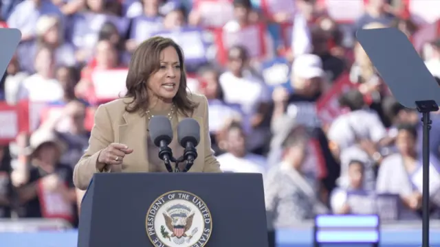 Kamala Harris speaks on stage at a rally in Atlanta. She is wearing a tan suit.