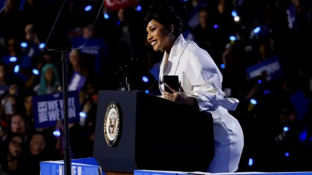 Cardi B stands on a podium in a white dress