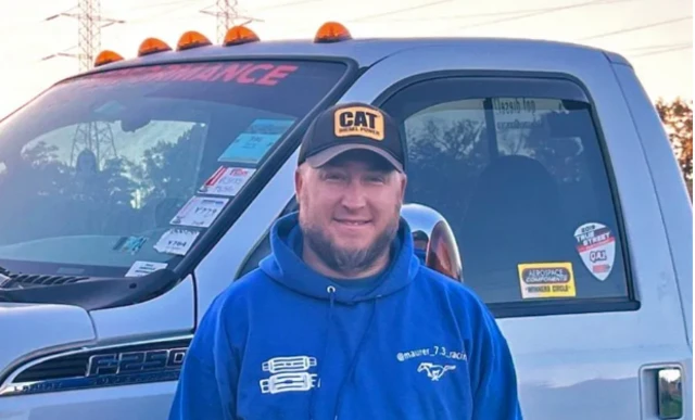 Ben Maurer smiles at the camera. He wears a black cap and a blue hoodie.