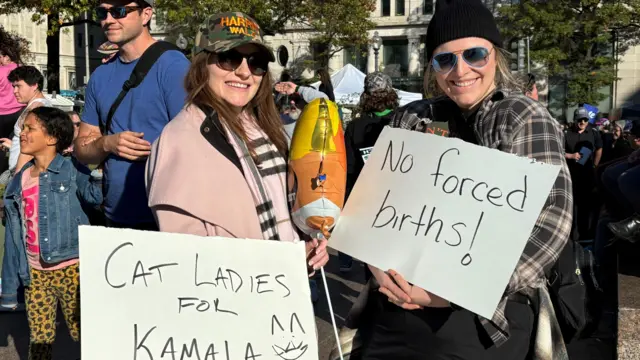 Two women holding signs reading 'Cat ladies for Kamala' and 'No forced births'