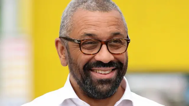 James Cleverly in front of a blurred yellow background